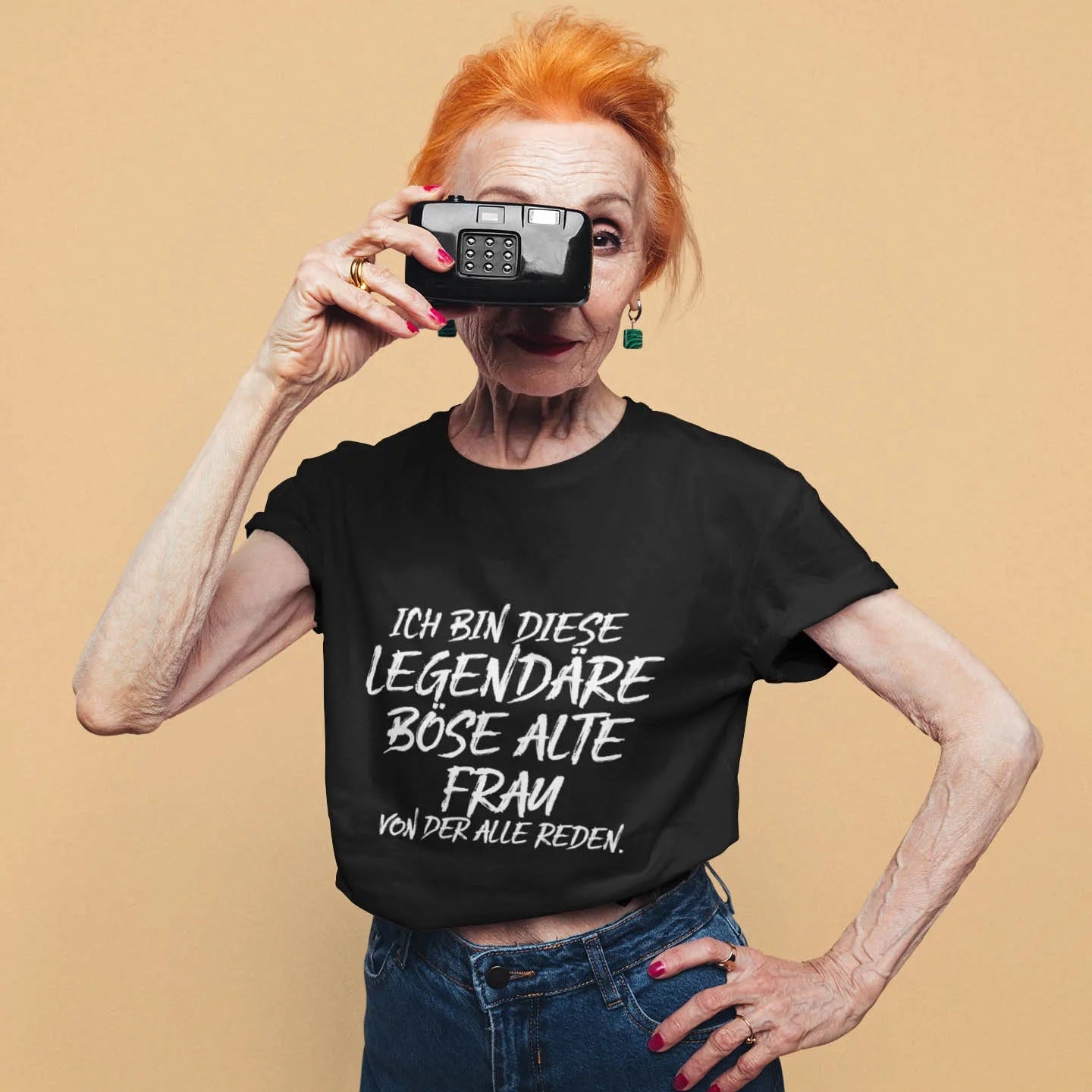Ältere Frau mit Kamera trägt schwarzes T-Shirt mit Statement „Ich bin diese legendäre böse alte Frau, von der alle reden“ – humorvolle Damenmode.